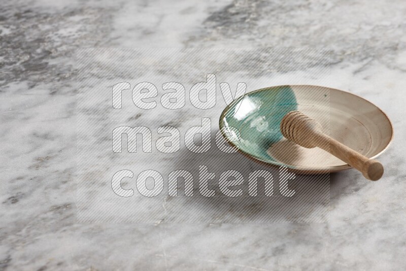 Multicolored pottery plate with wooden honey dipper in it on grey marble background