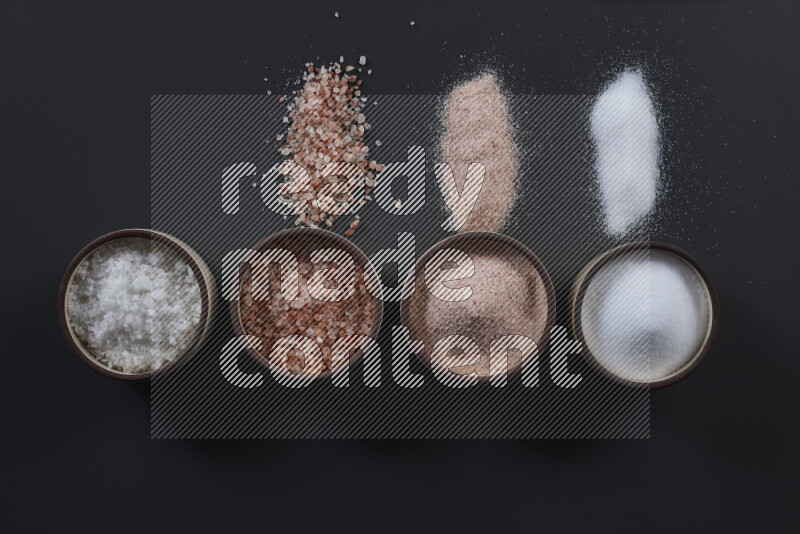 4 pottery bowls filled with himalayan salt and white salt on black background