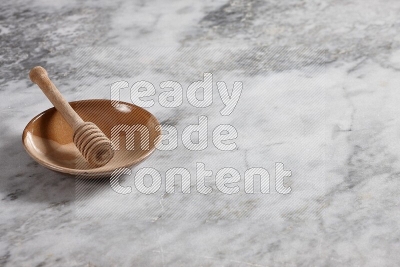 Multicolored pottery plate with wooden honey dipper in it on grey marble background