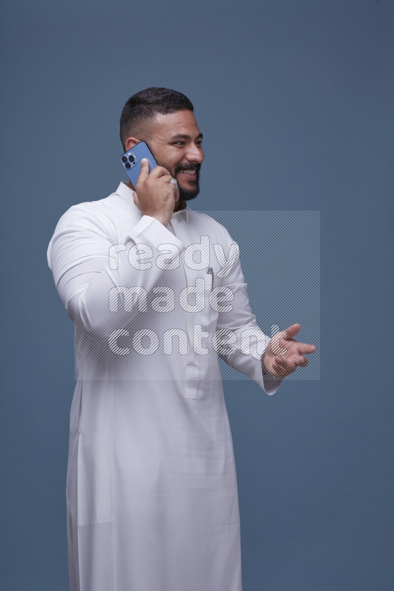 A Saudi man calling on blue background wearing Saudi Thob