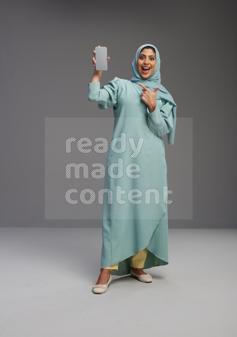 Saudi Woman wearing Abaya standing showing phone to camera on Gray background