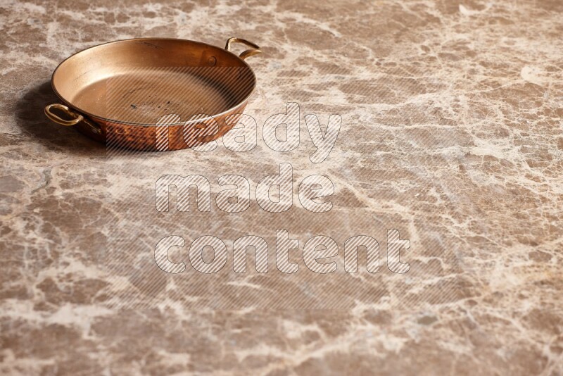 A small copper pan on beige marble background