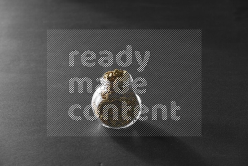 A glass spice jar full of cardamom on black flooring