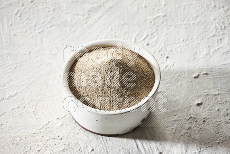 white pottery bowl full of white pepper powder on textured white flooring