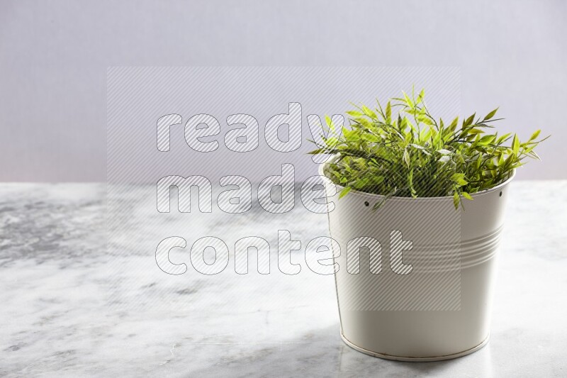 Green artificial plant in white pot on light grey marble background