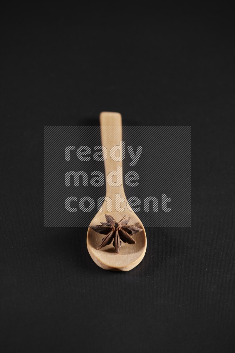 Star Anise in a wooden spoon on more stars anise filling the frame on black flooring