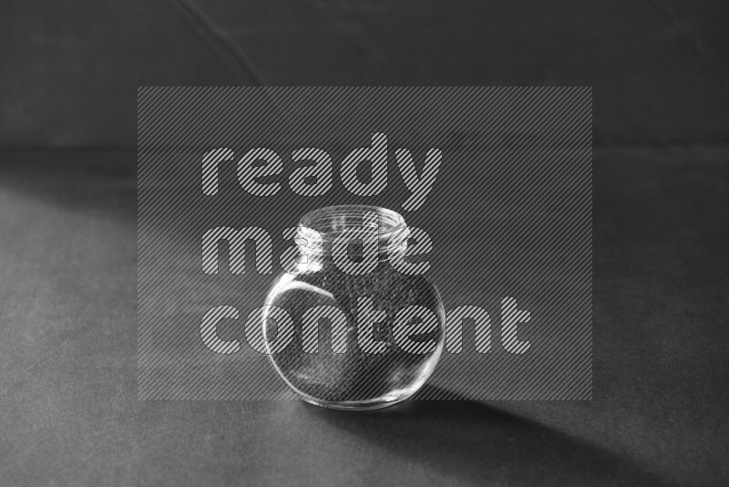 A glass spice jar full of black seeds on black flooring