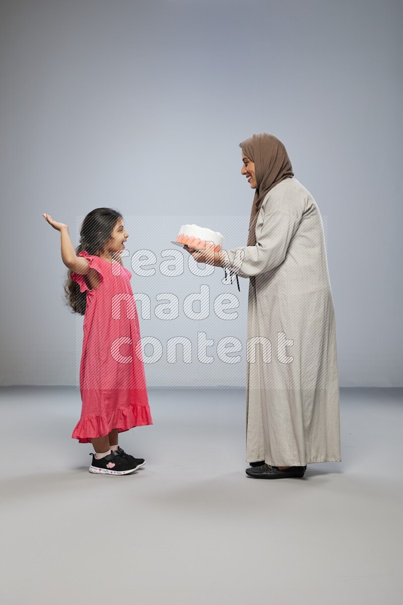 A mother giving a cake to her daughter on gray background