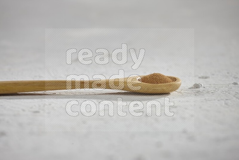 Cinnamon powder in a wooden spoon on a white background