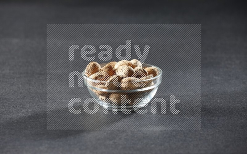 A glass bowl full of almonds on a black background in different angles
