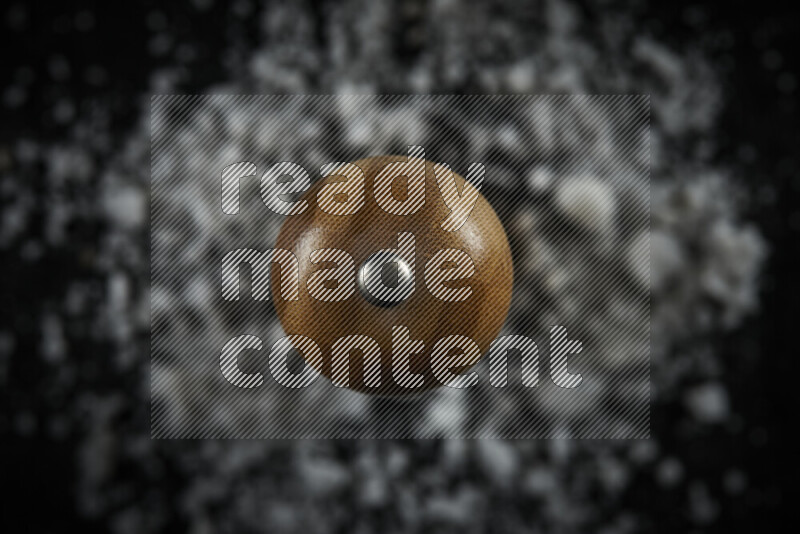 مطحنة خشبية قائمة بشكل عمودي محاطه بملح الطعام الأبيض الخشن علي خلفية سوداء