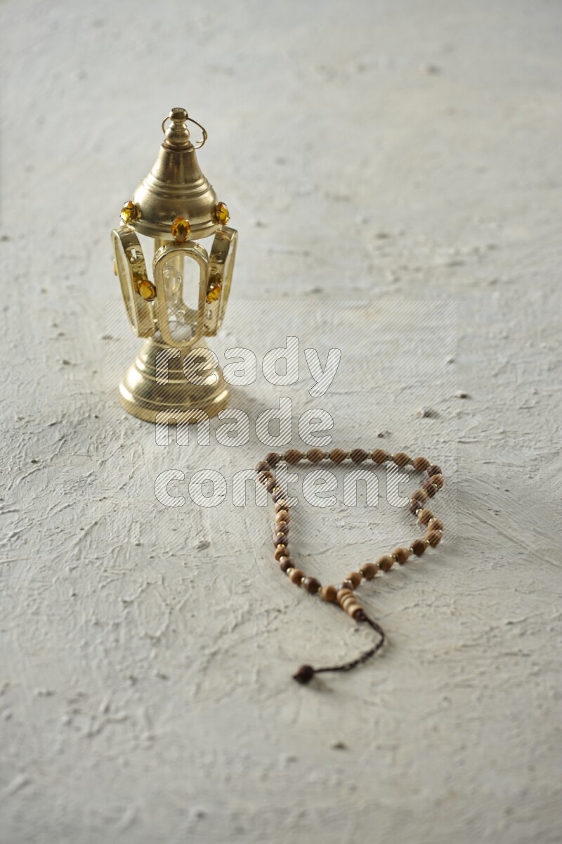 A golden lantern with different drinks, dates, nuts, prayer beads and quran on textured white background