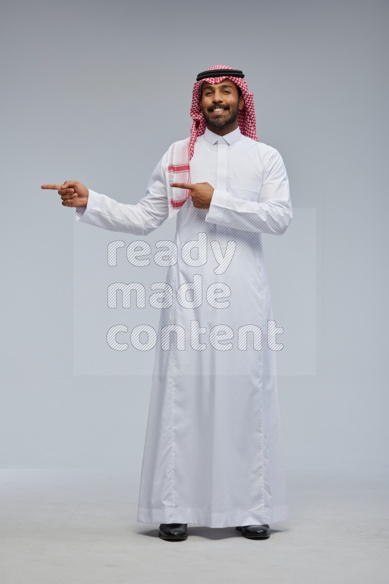 Saudi man Wearing Thob and shomag standing interacting with the camera on Gray background