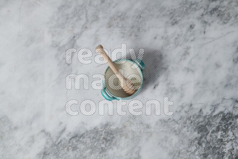 Multicolored pottery bowl with wooden honey dipper in it on grey marble background