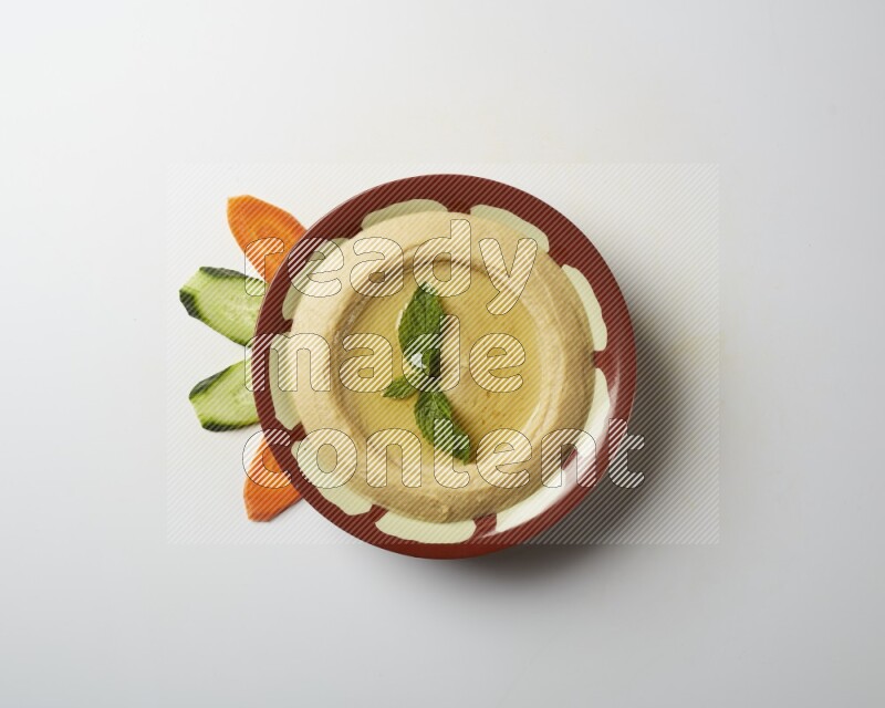 Hummus in a traditional plate garnished with mint on a white background