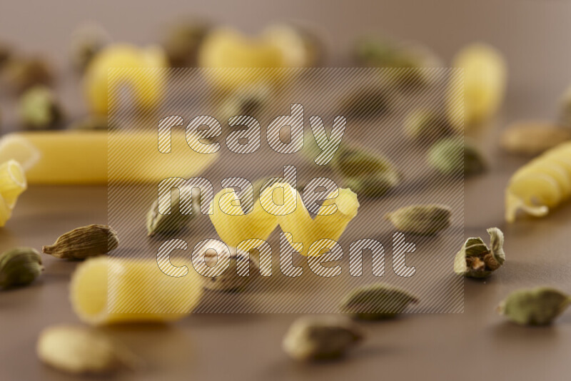 Raw pasta with different ingredients such as cherry tomatoes, garlic, onions, red chilis, black pepper, white pepper, bay laurel leaves, rosemary and cardamom on beige background