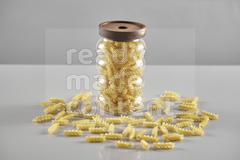 Raw pasta in a glass jar on light grey background