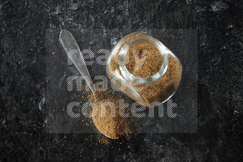 وعاء زجاجي للتوابل وملعقة معدنية ممتلئين ببودرة الكمون على خلفية سوداء