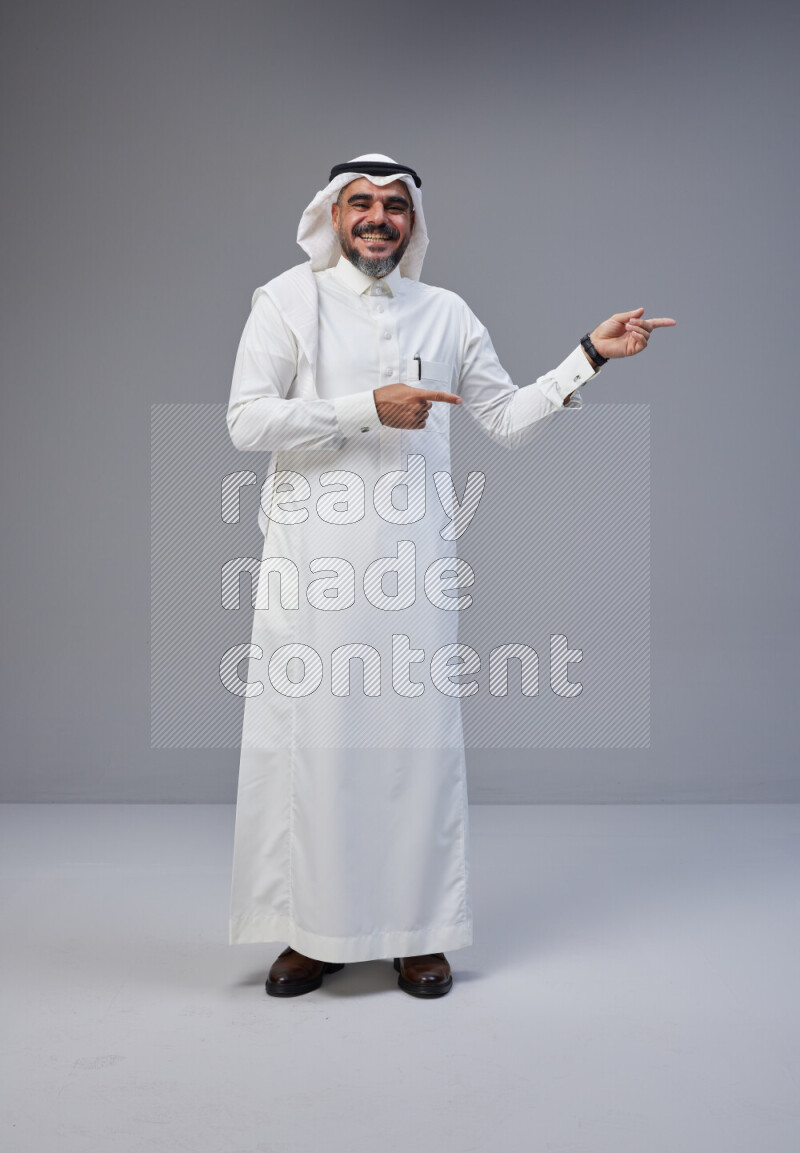 Saudi man Wearing Thob and white Shomag standing interacting with the camera on Gray background