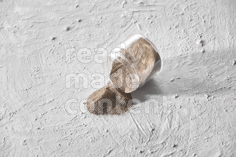 Flipped glass jar full of black pepper powder on a textured white flooring