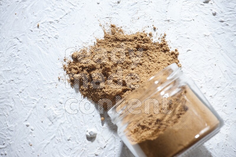 A flipped glass jar full of allspice powder and powder spilled out of it on a textured white flooring