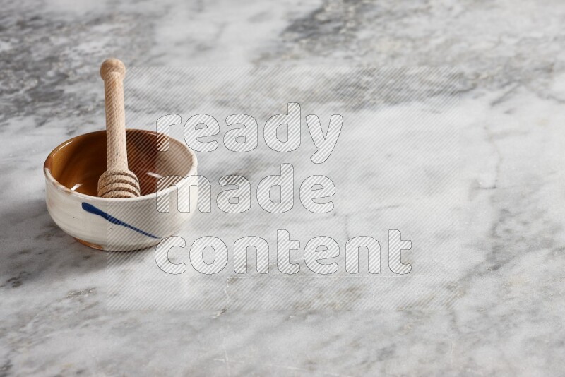 Multicolored pottery bowl with wooden honey dipper in it on grey marble background