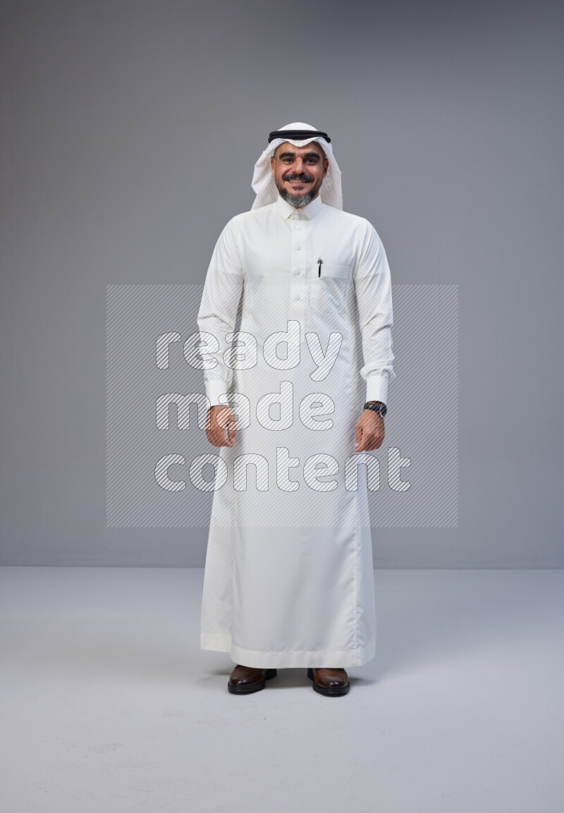 Saudi man Wearing Thob and white Shomag standing interacting with the camera on Gray background