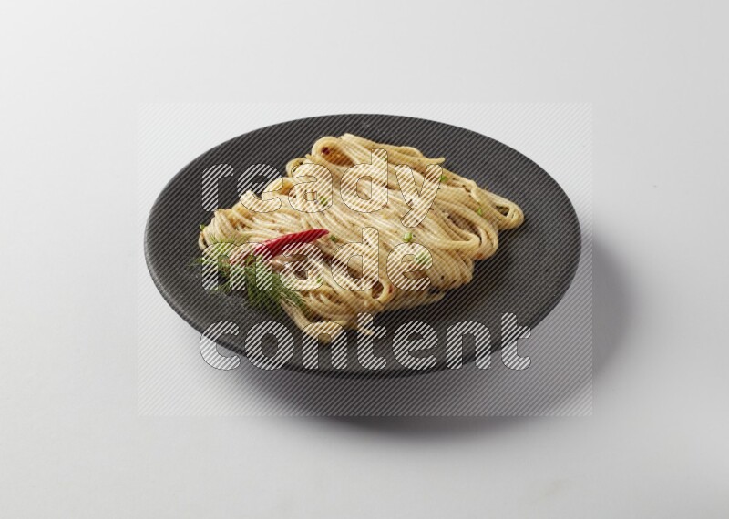 spaghetti pasta with white sauce on a black plate on a white background