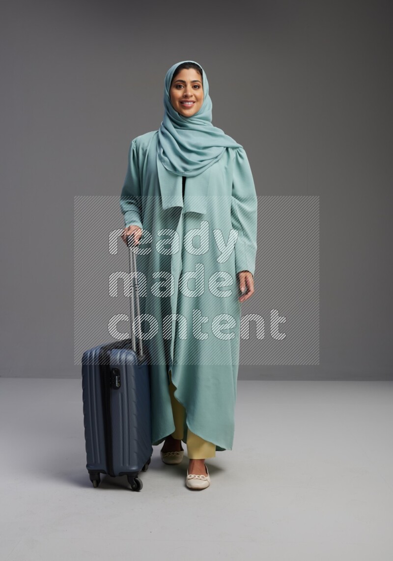 Saudi Woman wearing Abaya standing holding Travel bag on Gray background