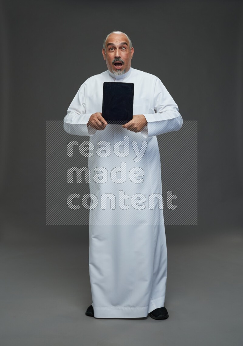 Saudi man without shomag Standing working on tablet on gray background