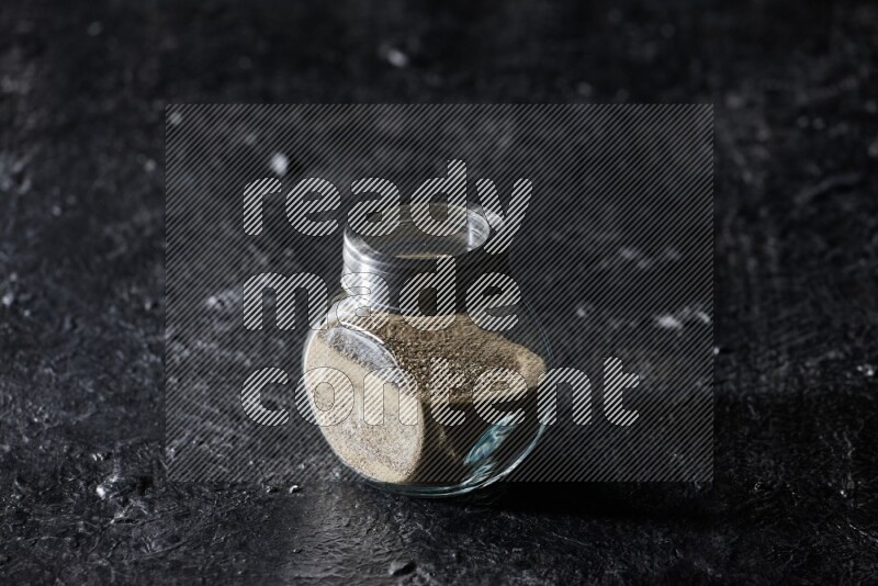 Herbal glass jar full of white pepper on textured black flooring
