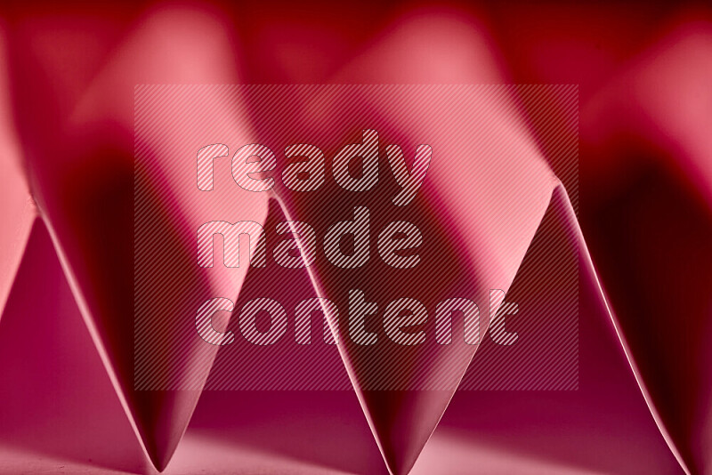 A close-up abstract image showing sharp geometric paper folds in red gradients