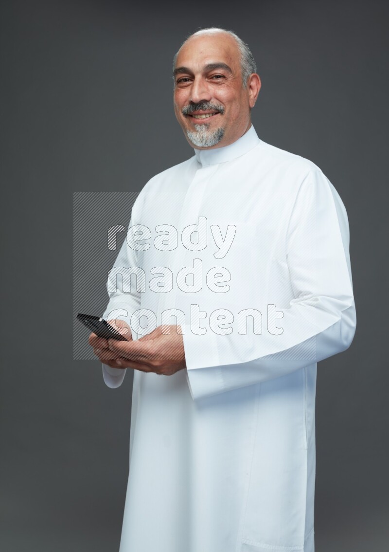 Saudi man without shomag Standing texting on phone on gray background