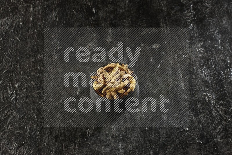 وعاء فخار أسود ممتلئ بأصابع كاملة من الكركم المجفف على خلفية سوداء