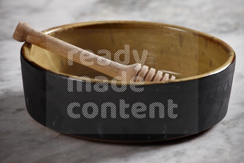 Multicolored pottery oven plate with wooden honey handle in it on grey marble background