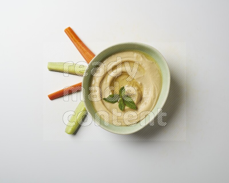 Hummus in a green plate garnished with mint on a white background