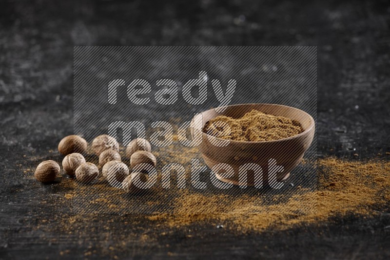 A wooden bowl full of nutmeg powder with the seeds and sprinkled powder beside it on a textured black flooring in different angles