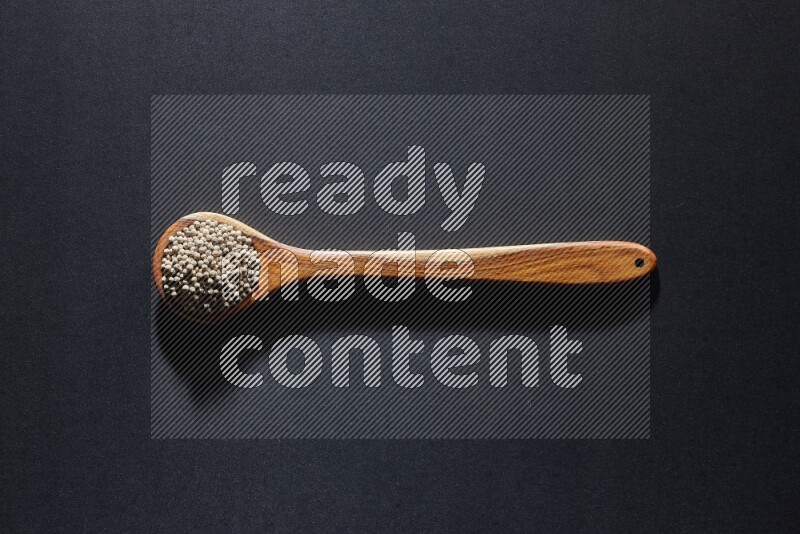 A wooden ladle full of white pepper beads on black flooring