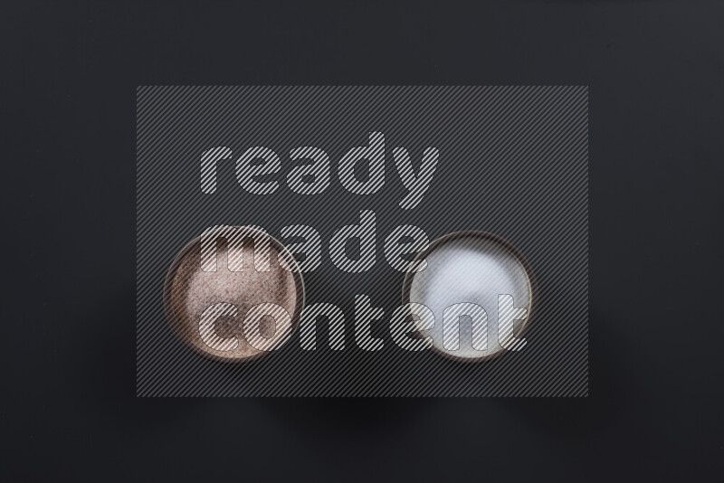 2 pottery bowls one is filled with himalayan salt and the other with white salt on black background