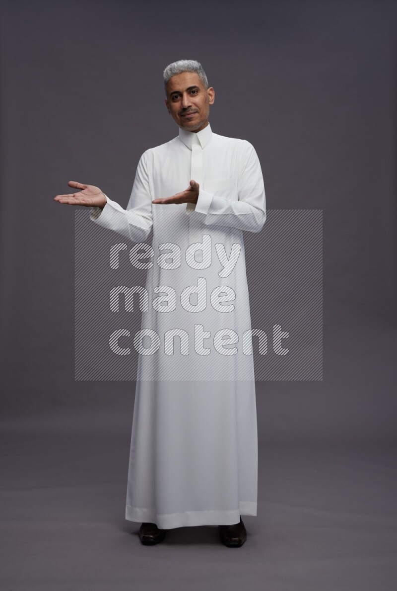 Saudi man wearing thob standing interacting with the camera on gray background