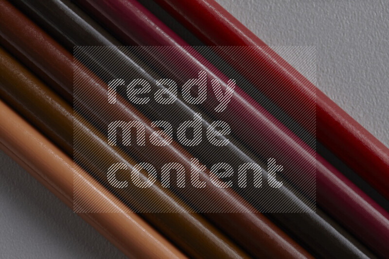 A collection of colored pencils arranged showcasing a gradient of brown hues on grey background