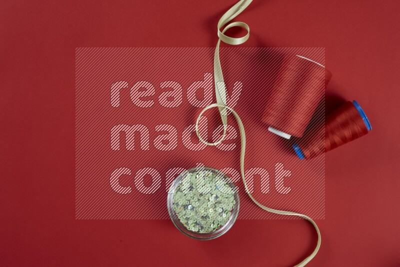 مجموعة من أدوات الخياطة والتفصيل خضراء وحمراء اللون على خلفية حمراء