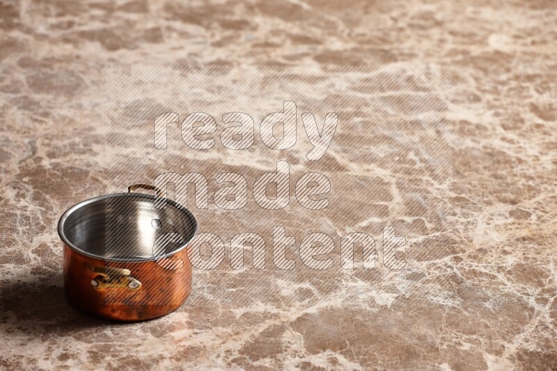 A small copper pot on beige marble background