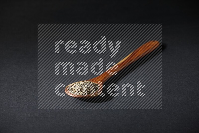 A wooden ladle full of cumin seeds on black flooring