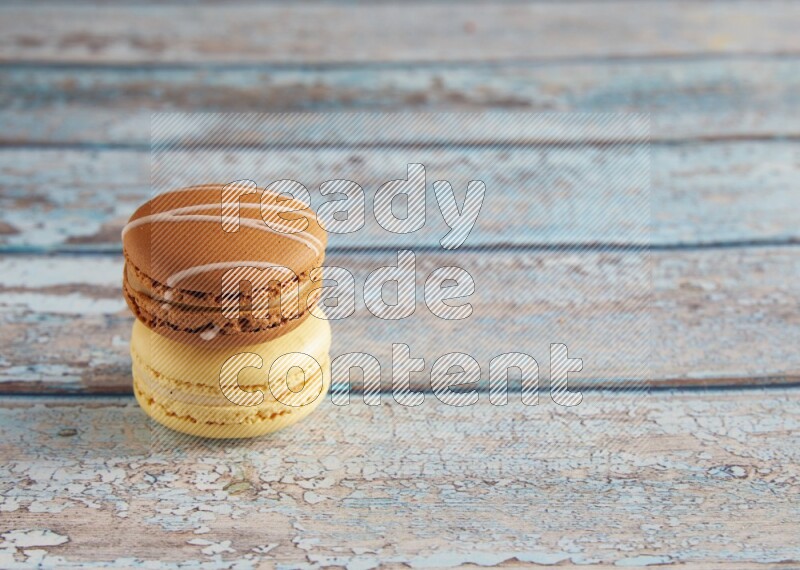 45º Shot of of two assorted Brown Irish Cream, and Yellow Vanilla macarons on light blue background