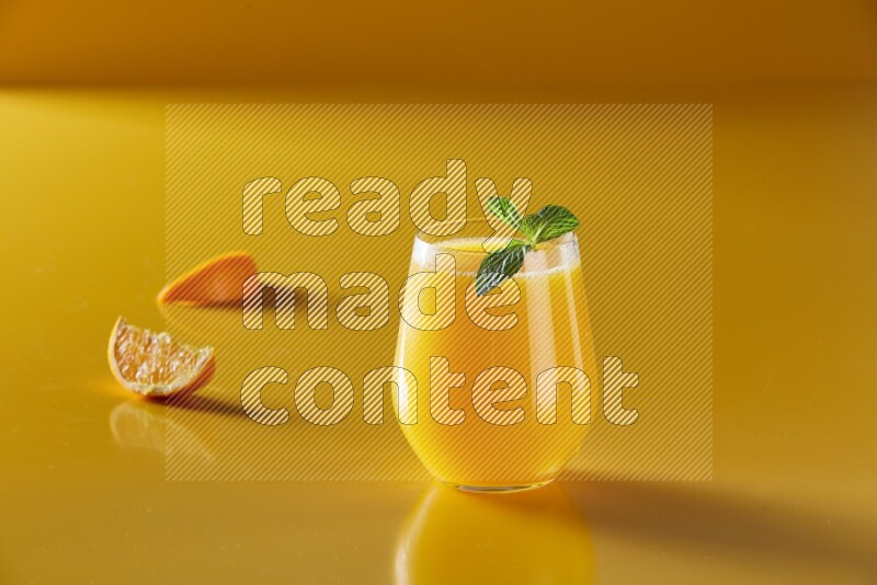 glass of orange juice with  mint on yellow background