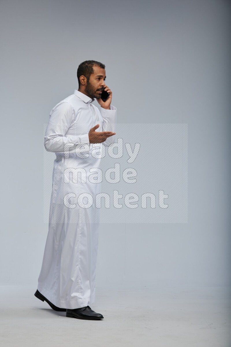 Saudi man wearing Thob standing talking on phone on Gray background