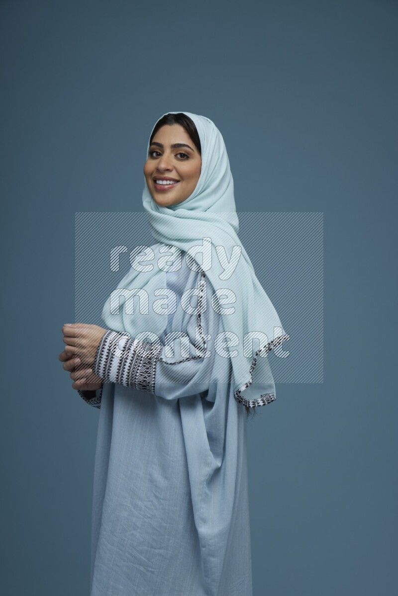 A woman posing in a blue background wearing a blue Abaya with hijab