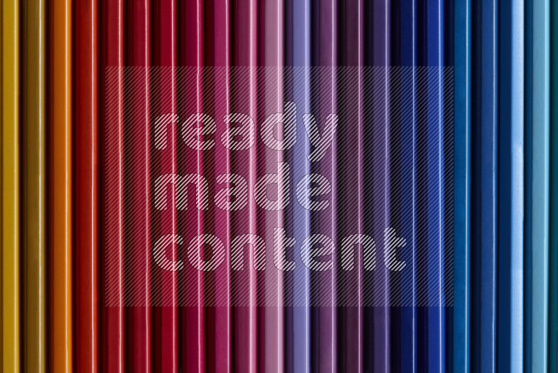A collection of colored pencils arranged showcasing a gradient of different hues on grey background