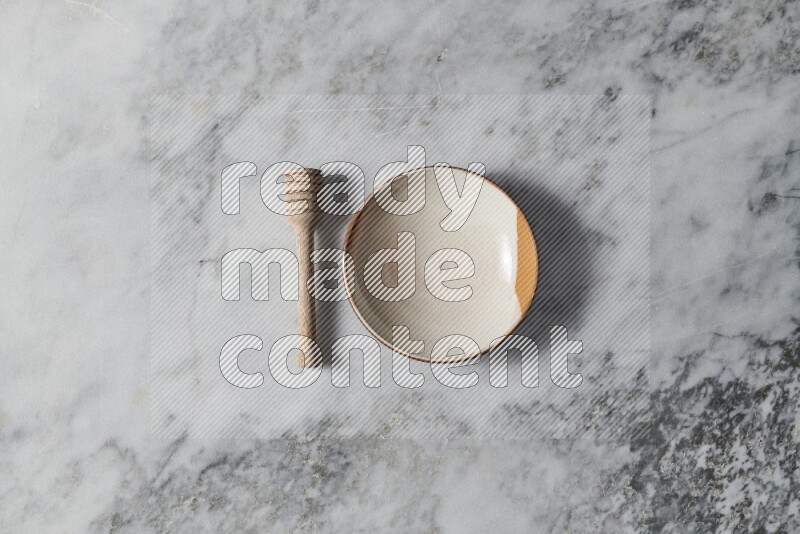 Multicolored pottery plate with wooden honey dipper on the side on grey marble background